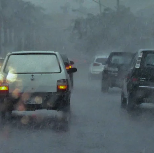 Foto de temporal com chuva intensa, com pontos de alagamento nas ruas e tráfego lento.
