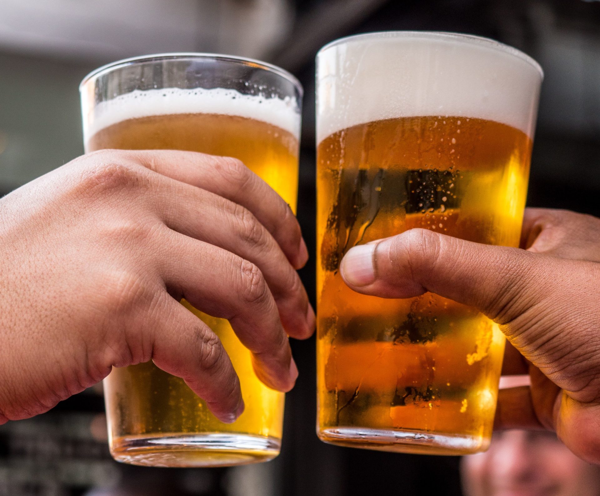 Cerveja convida a encontros reais. Duas mãos brindam com copos de cerveja