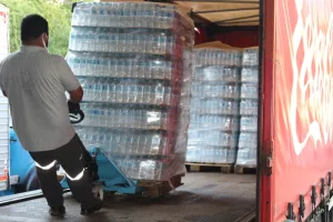 Coca-Cola, caminhão com garrafas de água. Um homem desloca garrafas em um carrinho.