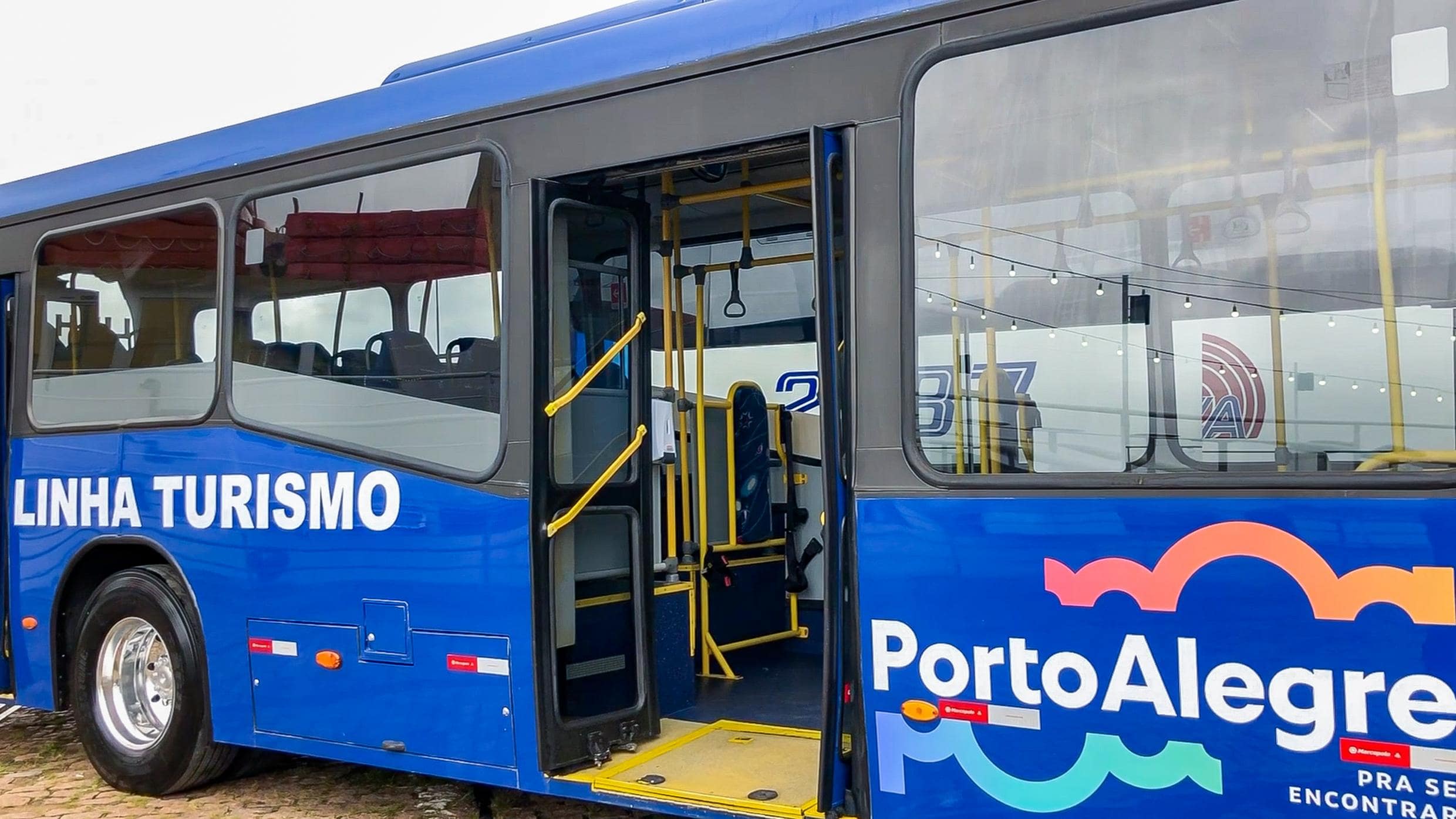 Ônibus da Linha Turismo, de Porto Alegre. O veículo é azul escuro e está com a porta central aberta.