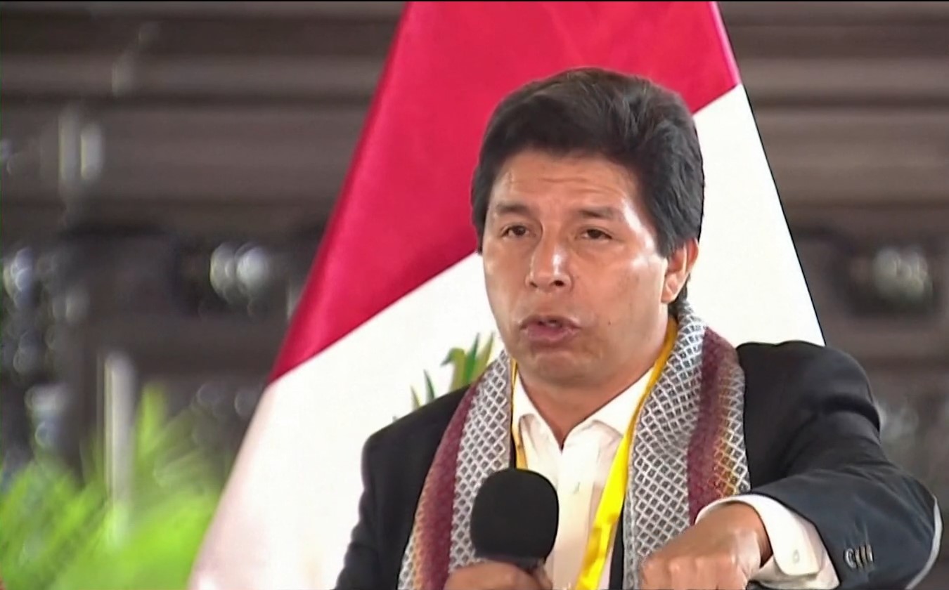 Pedro Castillo, presidente do Peru, discursa com microfone na mão direita. Ao fundo, a bandeira vermelha e branca do país latino-americano.