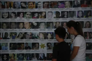 Mulher e menino olham para painel onde estão nomes e fotos das vítimas do incêndio na boate Kiss, em Santa Maria, no ano de 2013.