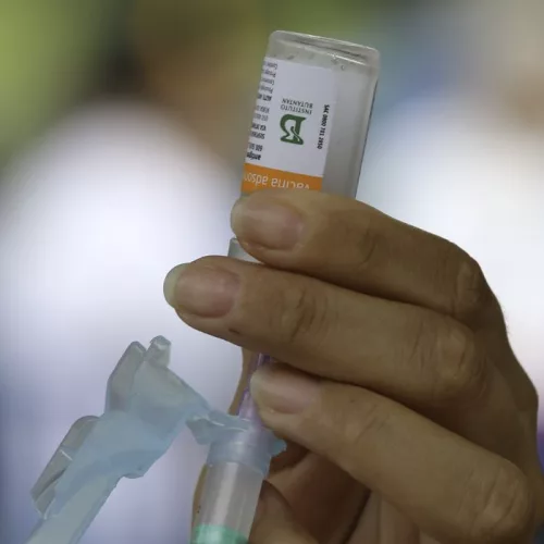 Mão de uma pessoa extraindo vacina de um frasco
