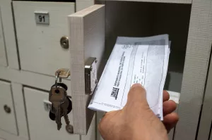 Uma pessoa pega, com a mão esquerda, uma conta do DMAE colocada em uma gaveta de um condomínio residencial.