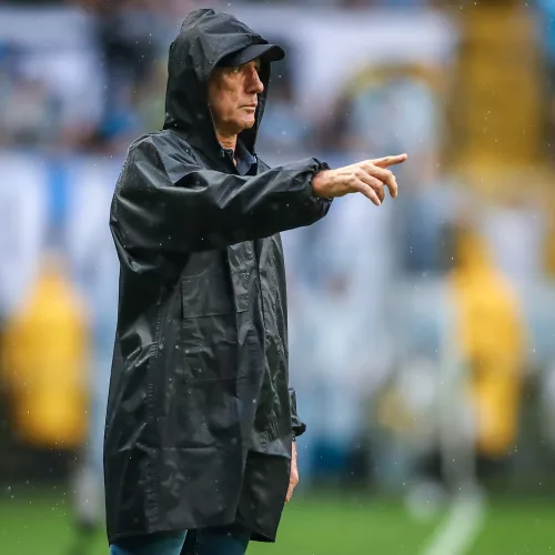 Renato à beira do campo, de capa de chuva preta, dando instruções à equipe do Grêmio